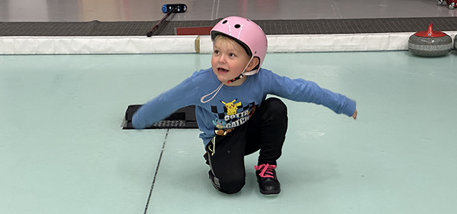 ett barn med hjälm glider på isen och håller ut armarna